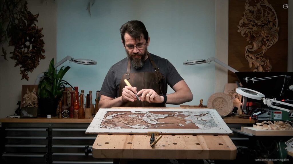 Immerse yourself in the artistry of Alexander Grabovetskiy as he skillfully demonstrates how to carve a furniture panel in this captivating image. His delicate craftsmanship on a walnut panel showcases the finesse and precision that only a master woodcarver possesses. For anyone eager to learn how to carve for furniture, this photograph stands as an invitation to embark on a fulfilling creative journey. Grabovetskiy, a luminary in the world of woodcarving, is renowned for his meticulous attention to detail. In this image, he is employing a repertoire of tools to transform a simple walnut panel into an artistic expression reminiscent of the opulent 18th-century style. The School of Wood Carving, led by Alexander Grabovetskiy, offers comprehensive woodcarving lessons. For those who cannot attend in person, the school also offers wood carving video workshops. These workshops, under the expert guidance of Woodcarver Grabovetskiy, are designed to take you through the process of carving panels and furniture with grace and precision. Whether you are a beginner seeking to learn the fundamentals, or an experienced woodcarver aiming to hone your skills, these woodcarving lessons provide you with the knowledge and techniques needed to excel. Grabovetskiy’s deep understanding of textures, patterns, and tools is evident in this photograph as his hands deftly shape the walnut panel. Through the lessons offered at the School of Wood Carving, you can achieve the artistic expression and craftsmanship on display in this image. Under the tutelage of Alexander Grabovetskiy, discover how each cut, each contour, and each detail come together to form an exquisite piece that speaks of a bygone era.