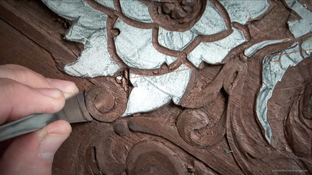 A person is using a carving tool to carve on a wood furniture panel.
