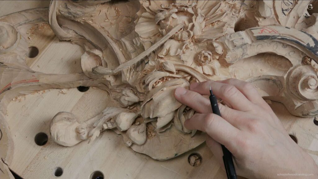 Close-up view of a hand holding a pencil, pointing at a meticulously crafted tulip flower featured on a Grinling Gibbons woodcarving. The woodcarving masterpiece showcases the detailed craftsmanship of woodcarving. Grinling Gibbons' woodcarving techniques are evident in the intricate design. The pencil underscores the precision involved in woodcarving. Tulip flower, a highlight of the woodcarving, depicts the realistic approach of Grinling Gibbons' woodcarving style. The woodcarving composition presents a harmonious blend of nature and art. An unmissable piece of woodcarving art demonstrating the timeless beauty of Grinling Gibbons' woodcarving legacy. The woodcarving reveals the artist's meticulous attention to detail. This woodcarving is a testament to the skills required in creating such intricate works of art. Explore the depth and texture of this stunning example of Grinling Gibbons' woodcarving prowess.