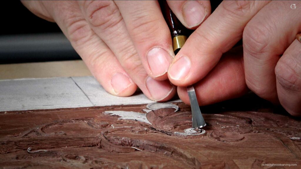 Craftsperson carving intricate patterns into wood with a chisel.