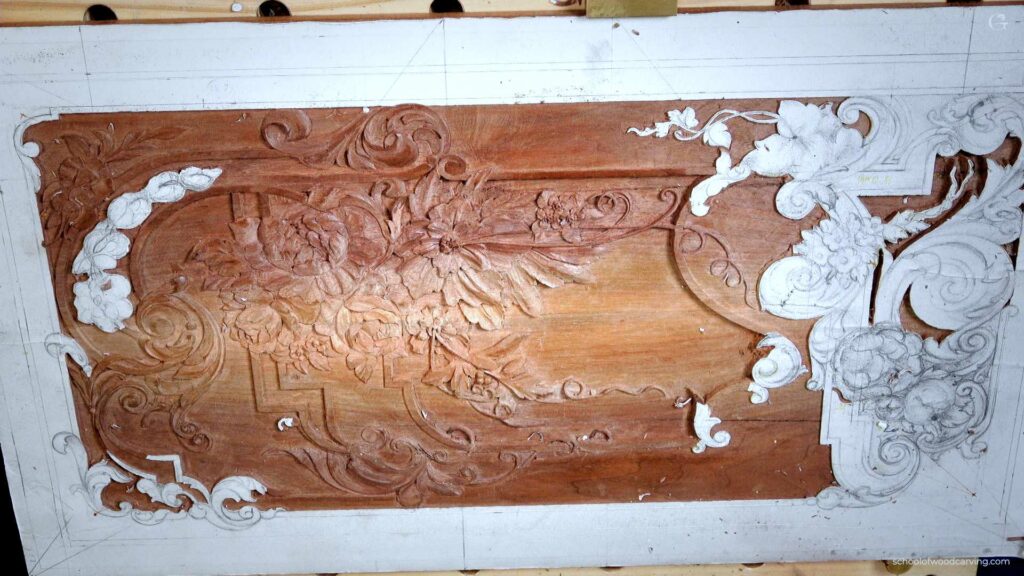 Intricately carved wooden panel featuring floral designs, partially unfinished with visible wood shavings.