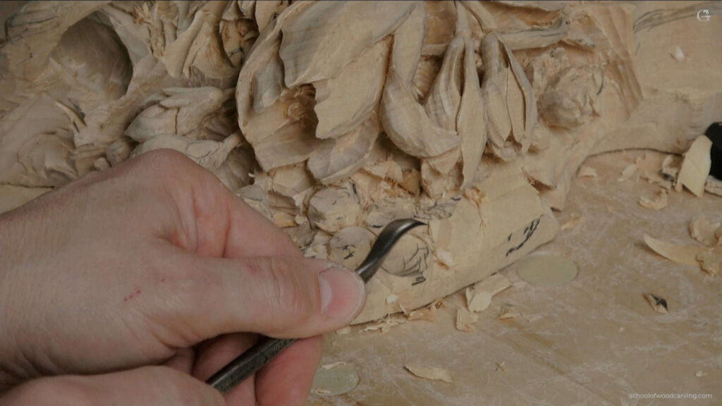 WOODCARVING LESSONS: A close-up photo shows Woodcarver Grabovetskiy holding a carving tool. He carefully carves detailed flower and leaf shapes into wood. You can see wood shavings and carved patterns on the wood’s surface. The table has small pieces of wood scattered around. Learn how to carve beautiful designs with expert Woodcarver Grabovetskiy in our easy-to-follow woodcarving lessons or course. See the tools, clear carving steps, and tips for beginners in every tutorial picture. - Wood Carving tutorials