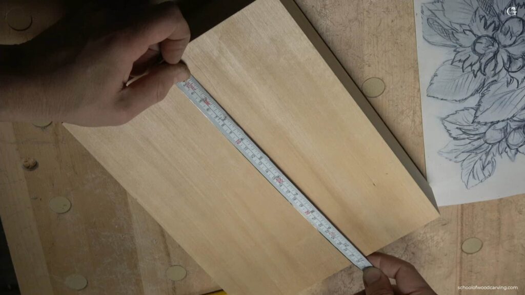 WOODCARVING LESSONS: Woodcarver Grabovetskiy measures a wooden board’s width with a tape. Hazelnut sketch for woodcarving is seen on white paper nearby. - Wood Carving tutorials